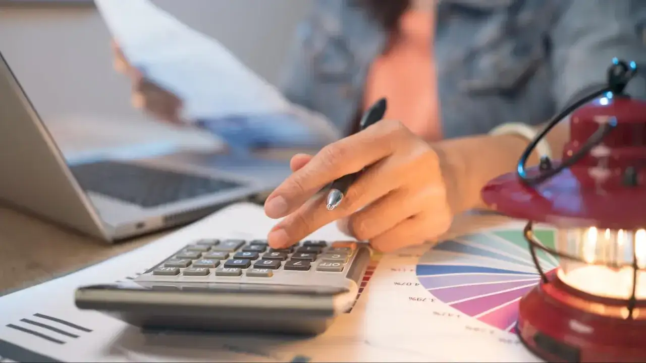 Persona calcula con calculadora y port&aacute;til, revisando gr&aacute;ficos. Quiz&aacute;s planeando una hipoteca puente Santander.
