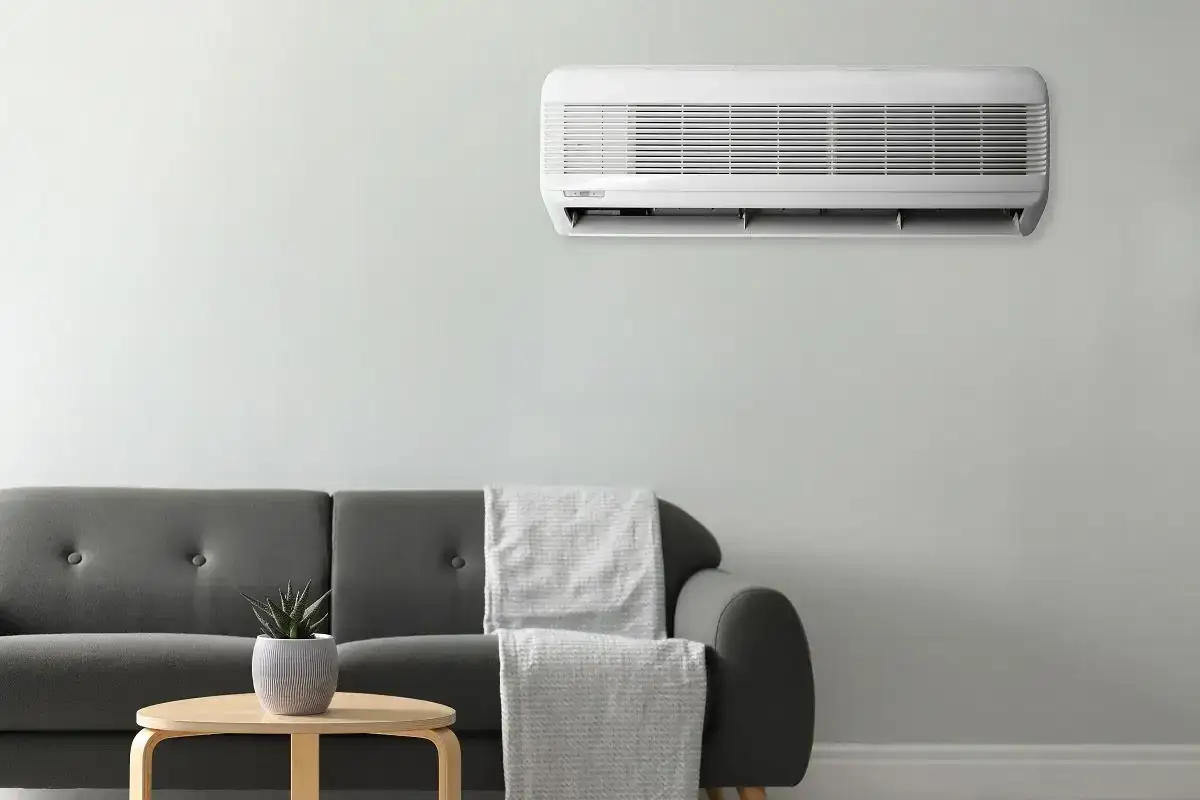 Un aire acondicionado blanco montado en la pared sobre un sofá gris. Averigua cuanto vale instalar un aire acondicionado para tener un hogar fresco.