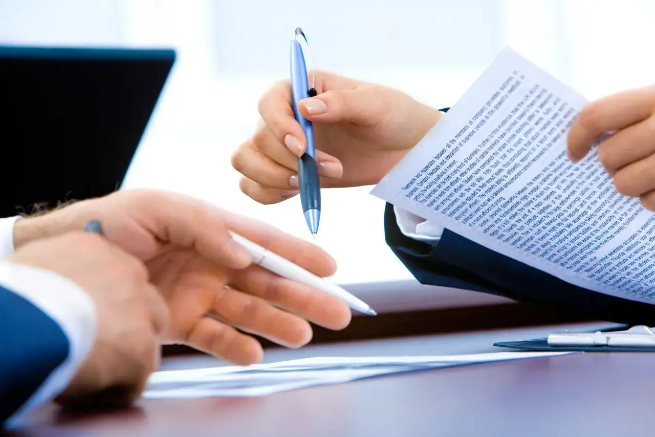 Manos revisando documentos y bolígrafos, discutiendo cómo vender piso con hipoteca.