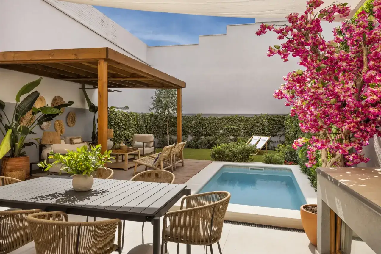 Un patio moderno con piscina azul, zona de comedor y pérgola. Ideal para relajarse y disfrutar del buen tiempo. Pregúntate: cuanto cuesta hacer una piscina así.