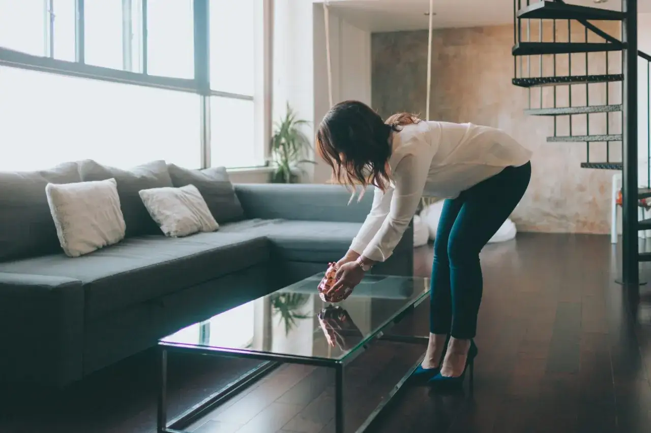 Mujer arregla un objeto decorativo en una mesa de cristal, preparando su hogar para vender un piso r&aacute;pido.