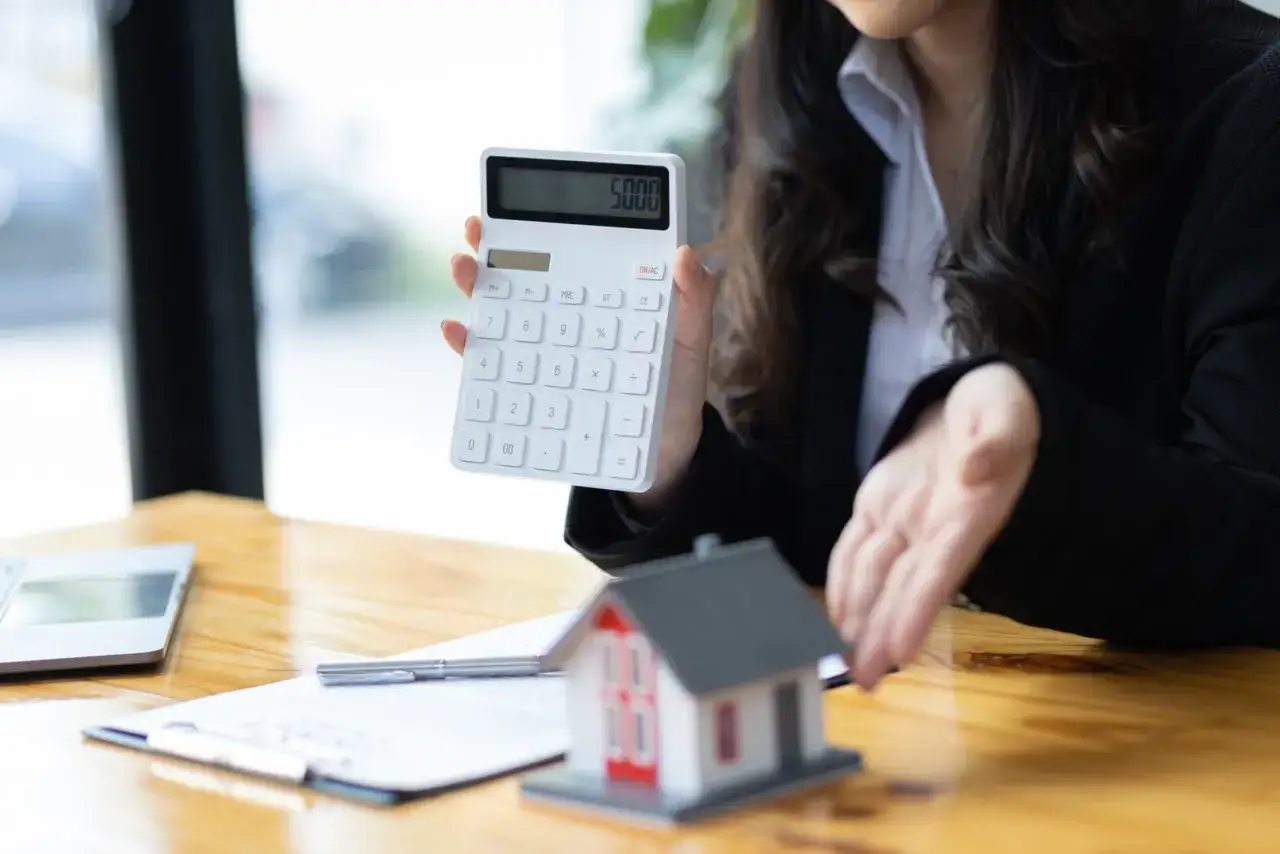 Calculando los gastos de compra de vivienda en Madrid. Una calculadora muestra 5000, junto a una maqueta de casa.