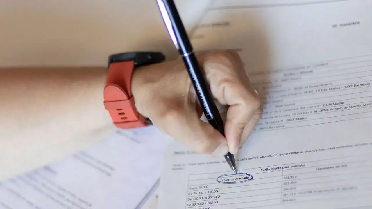 Mano con reloj naranja escribe en documento. Se resalta 