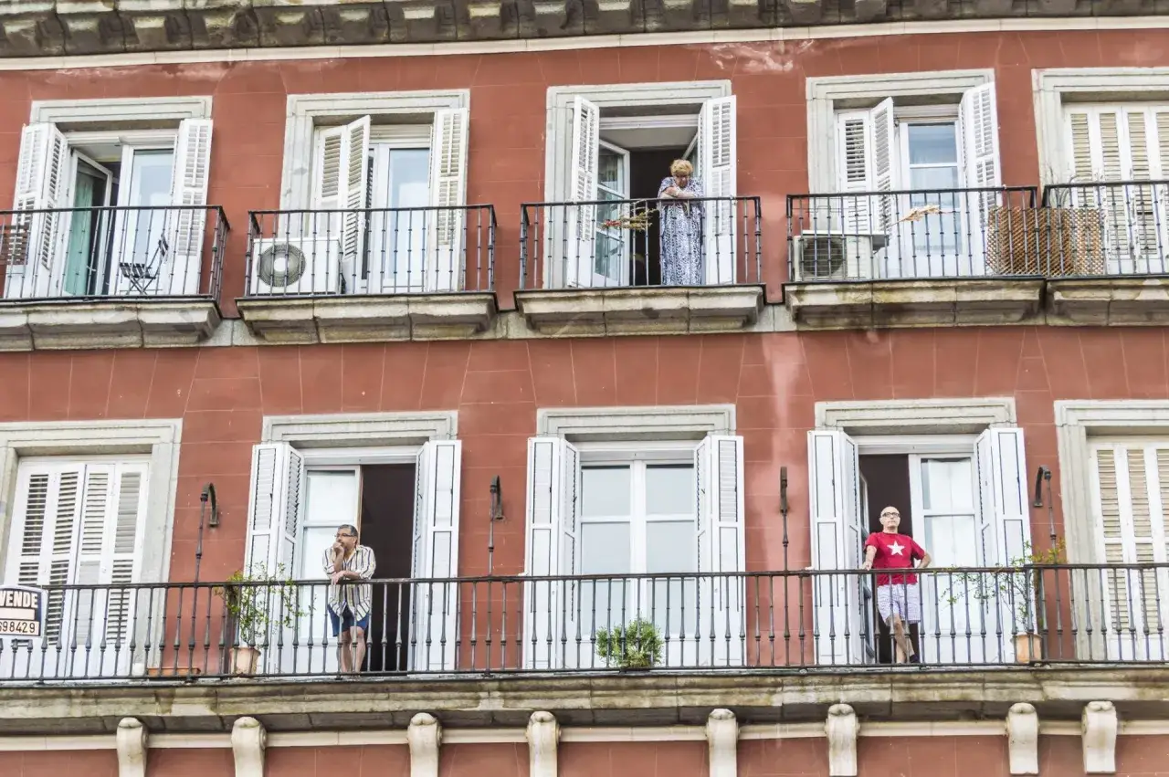 Personas en balcones de edificio con fachada rojiza, un recordatorio de la ley de propiedad horizontal y la convivencia vecinal.