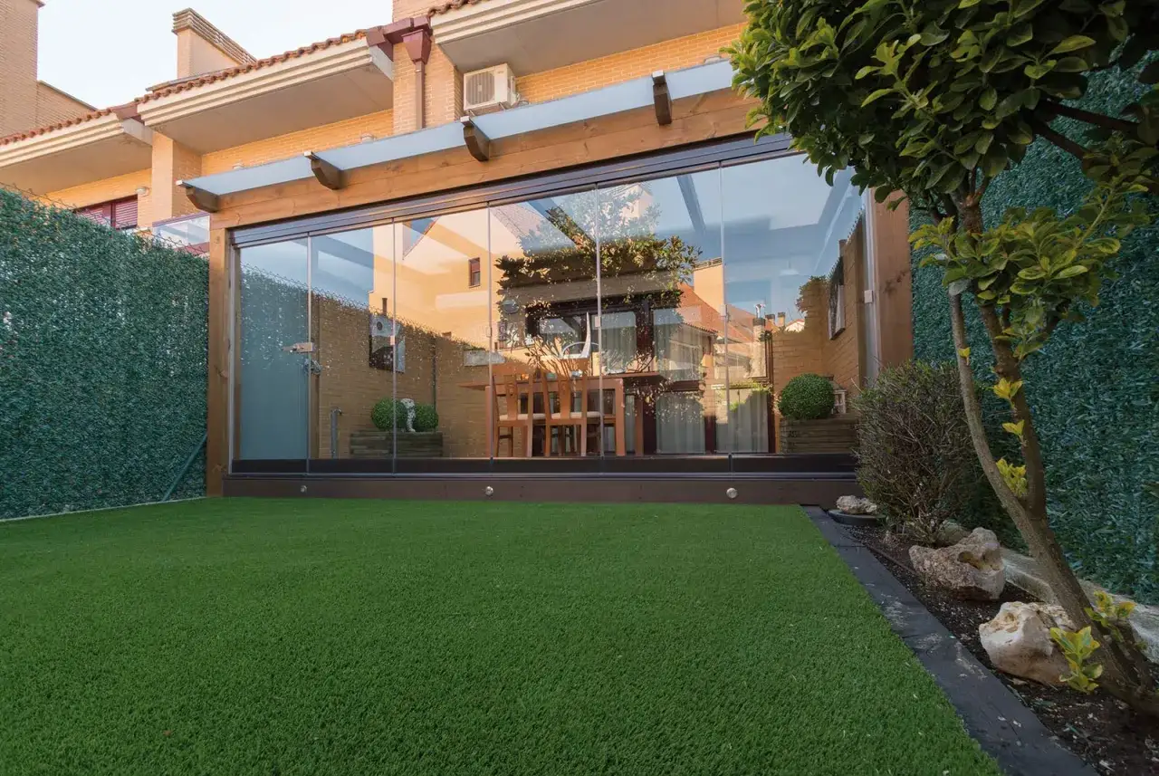 Cerramiento terraza casa unifamiliar con cristaleras y césped artificial. Un espacio moderno y luminoso para disfrutar del exterior.