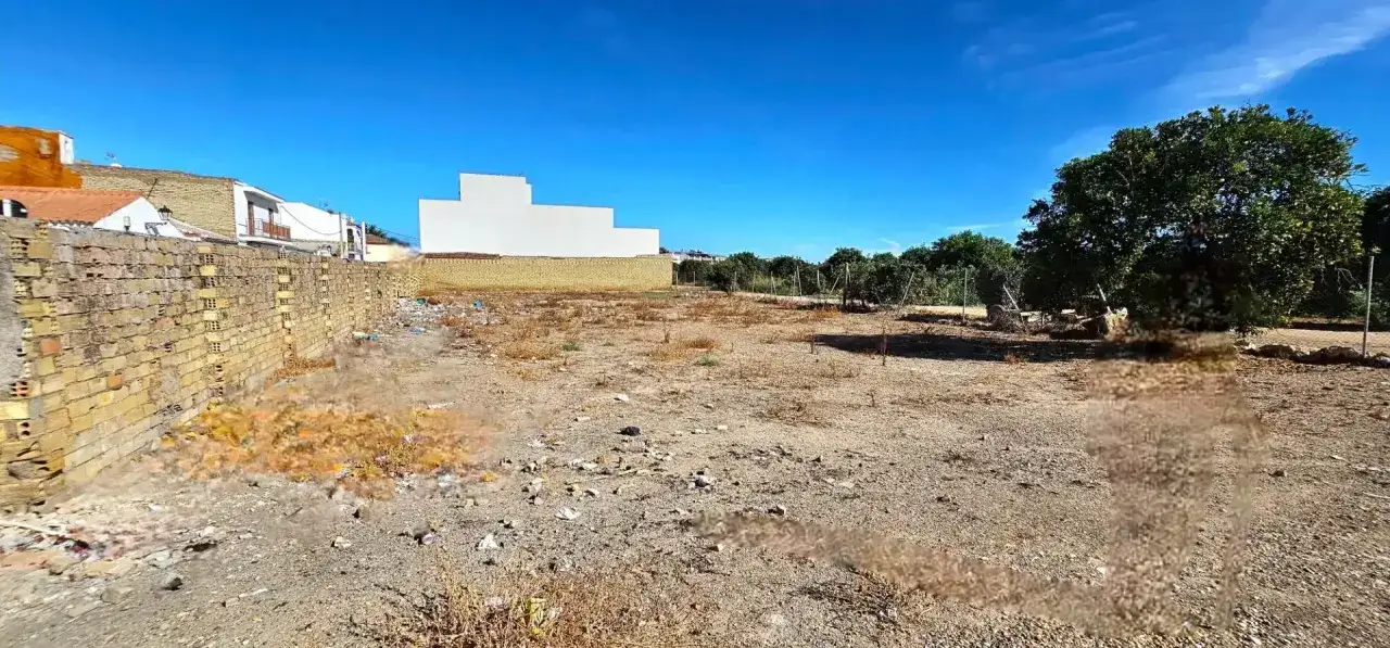 Un terreno es un bien inmueble con una pared de ladrillos, casas al fondo y árboles.
