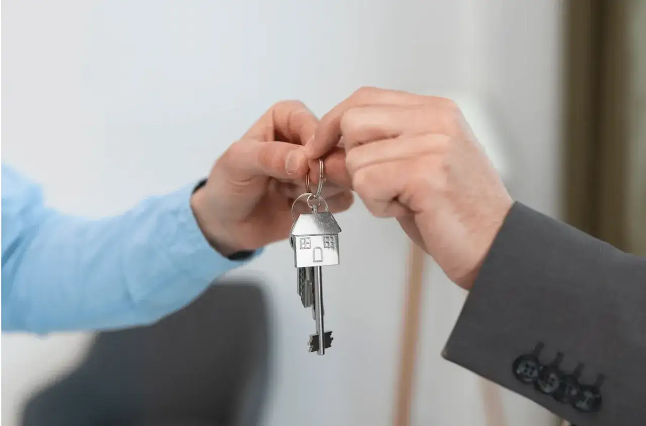 Manos entregando llaves con un llavero de casa, simbolizando la compra de una vivienda en España.