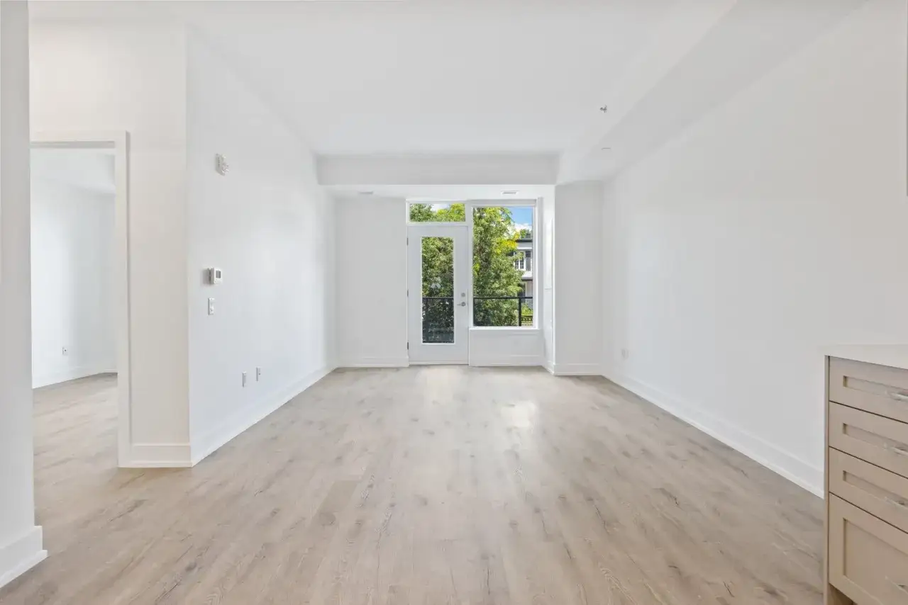 Salón luminoso con suelo de madera y puerta acristalada que da a un balcón. Ideal para entender como se declara la venta de un piso heredado.